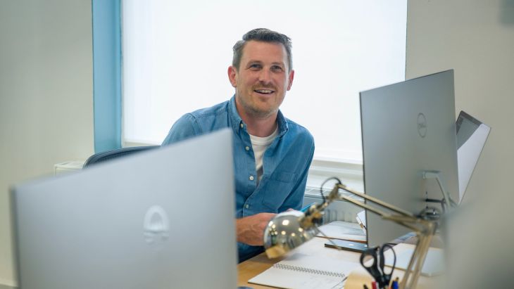 Andy sitting in the Brightec office smiling as he thinks about leading a remote team